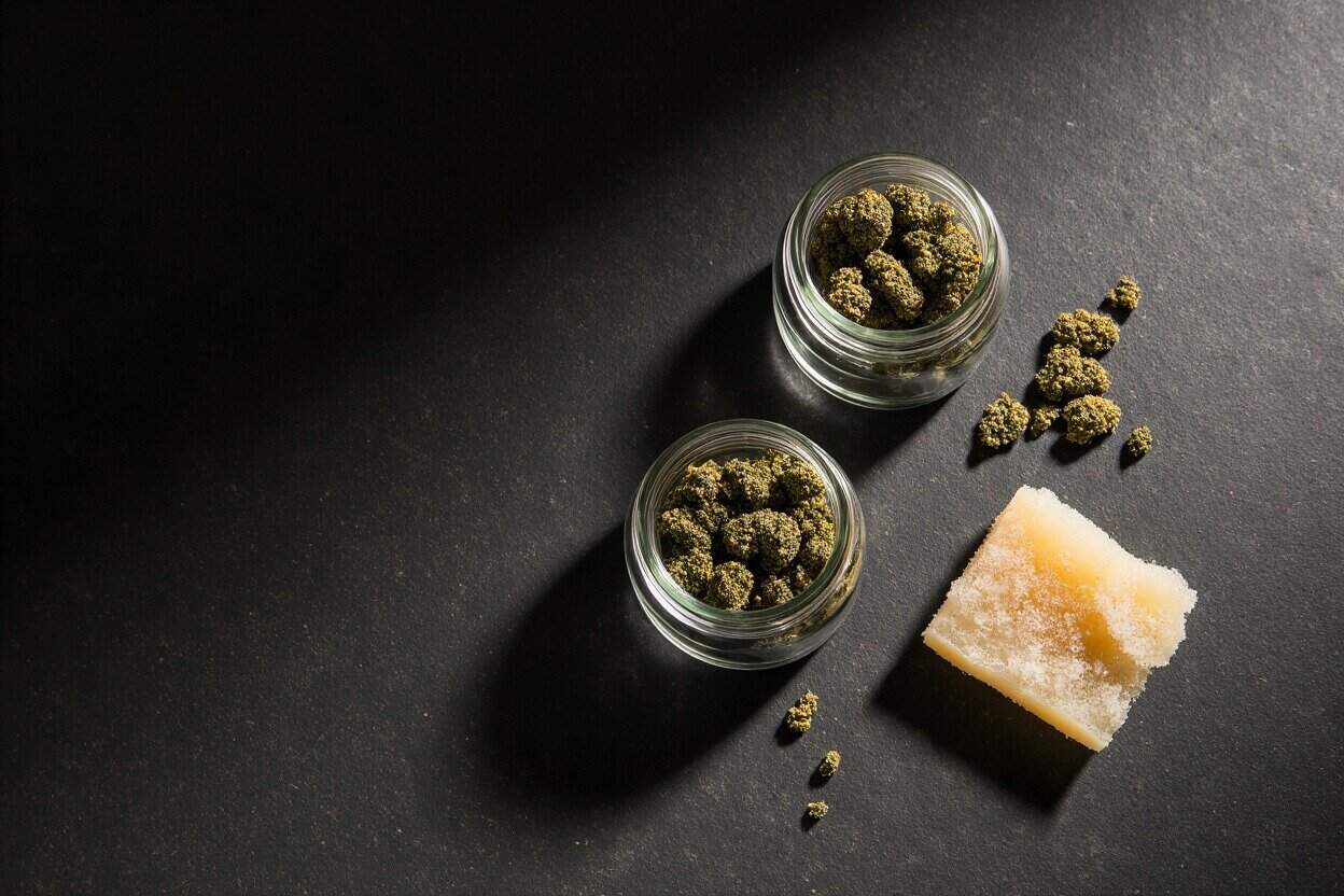 Premium Canadian cannabis buds in glass jars with a cannabis-infused soap bar on dark textured surface, highlighting high-quality strains from Great Canadian Buds for discerning consumers.