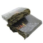 Close-up of a pressed cannabis brick wrapped in black plastic with red and gold branding, showcasing dense, potent marijuana typically sourced from trusted Canadian dispensaries.